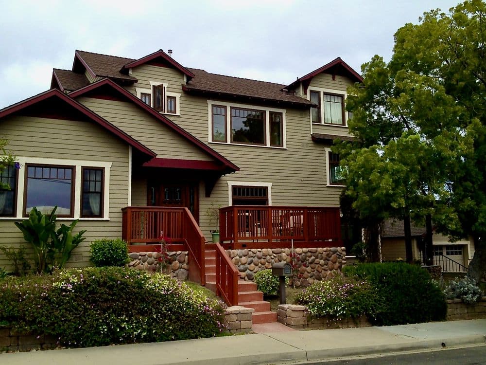Two-story house with a red trim, wooden deck, and landscaped front yard.