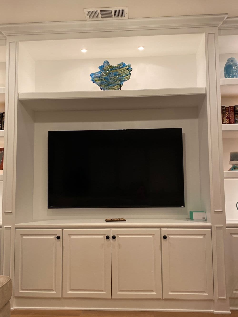 Modern living room with a large TV and decorative blue sculpture on a white shelf.