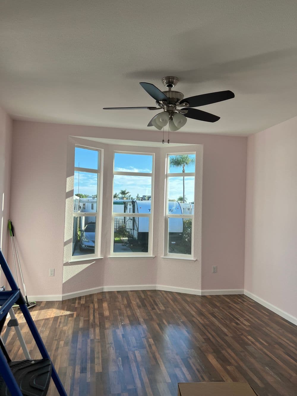 Modern room with pink walls, large windows, ceiling fan, and hardwood floor.