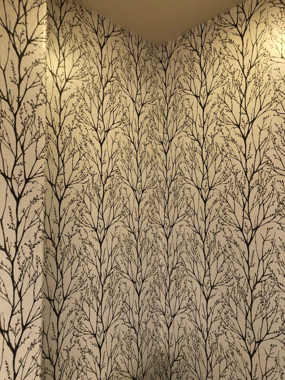 Black tree branch wallpaper pattern on a corner wall, creating a natural aesthetic.