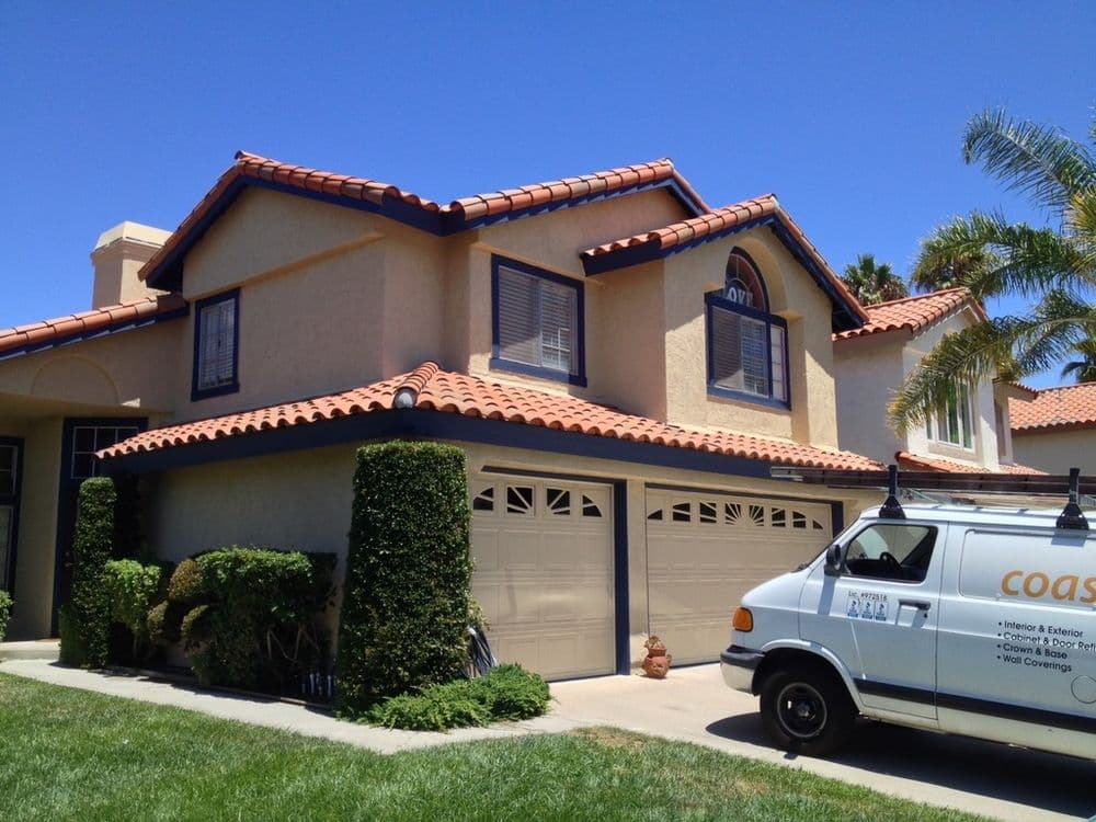 Two-story house with a tile roof, garage, and landscaping; service van parked in front.