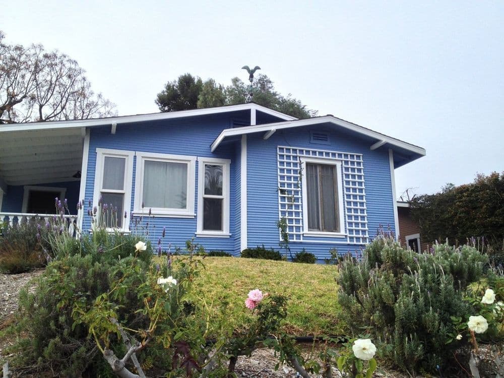 Blue house with lattice window and lush garden, surrounded by flowers and greenery.