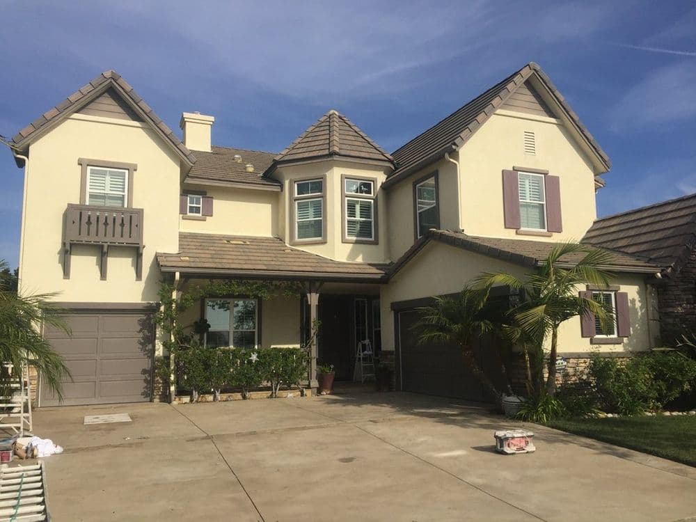 Two-story family house with a balcony, garage, and landscaped entrance on a sunny day.