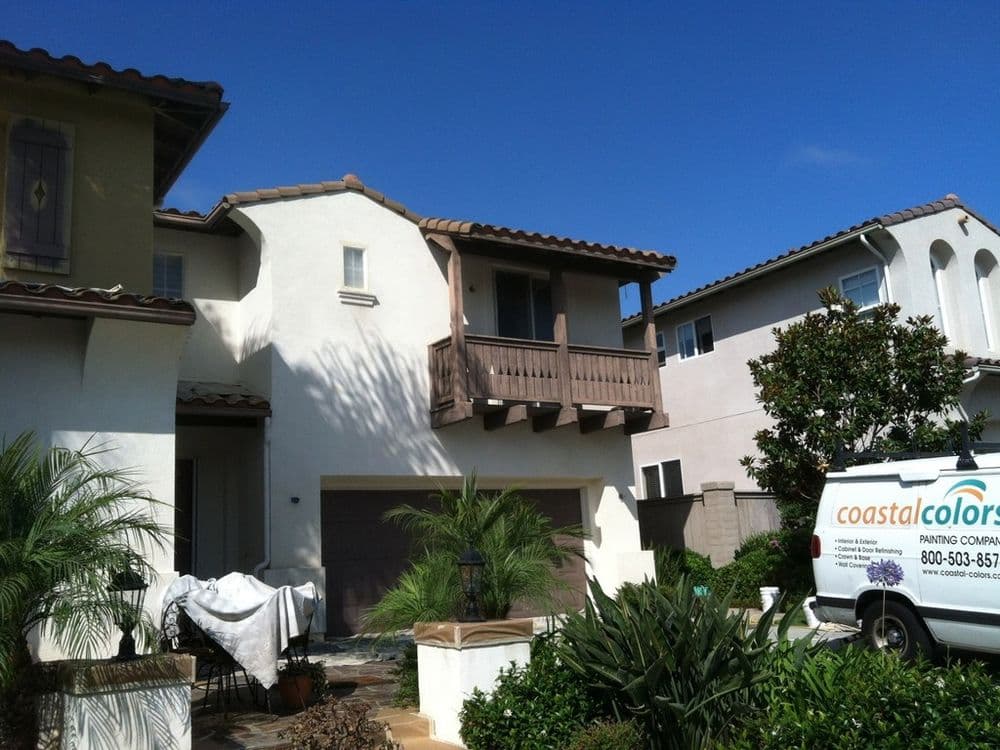Modern coastal home with balcony, surrounded by greenery and a painting company van.