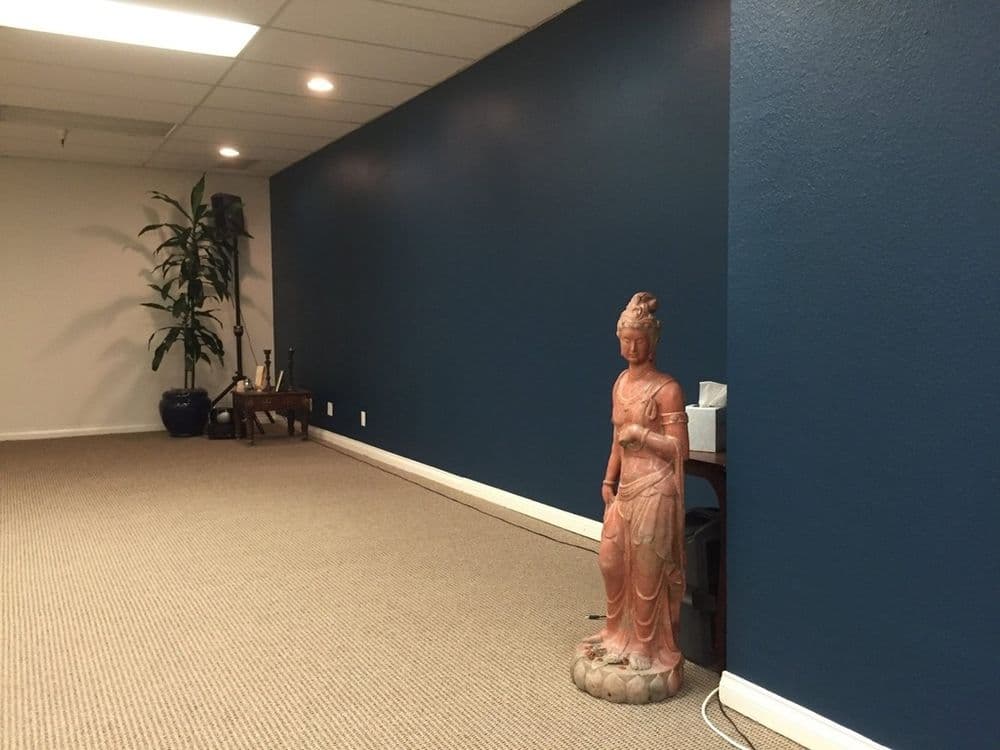 Buddha statue beside a plant in a serene, minimalist indoor space with blue walls.