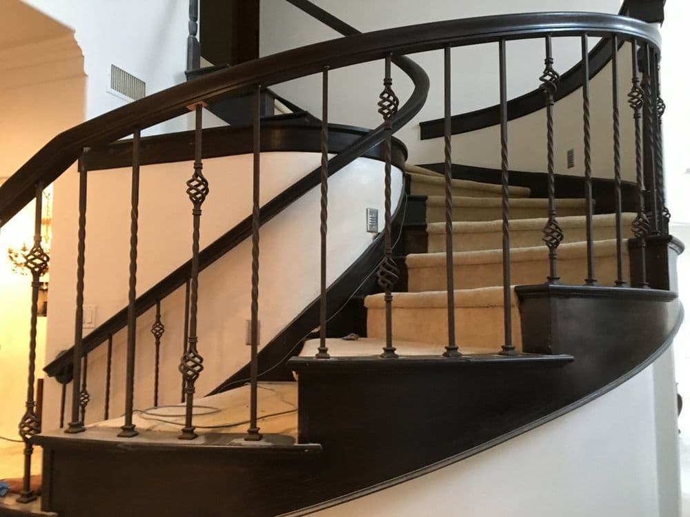 Elegant curved staircase with wrought iron railing and carpeted steps. Luxurious interior design.