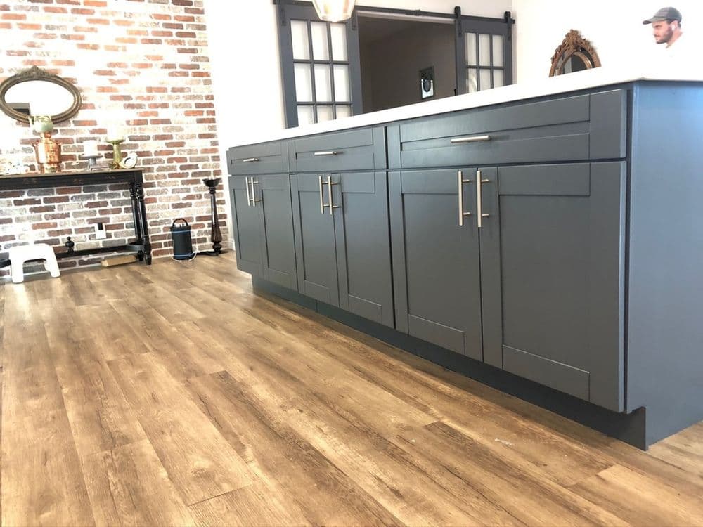 Modern kitchen with gray cabinets and wooden flooring, featuring a rustic brick wall.