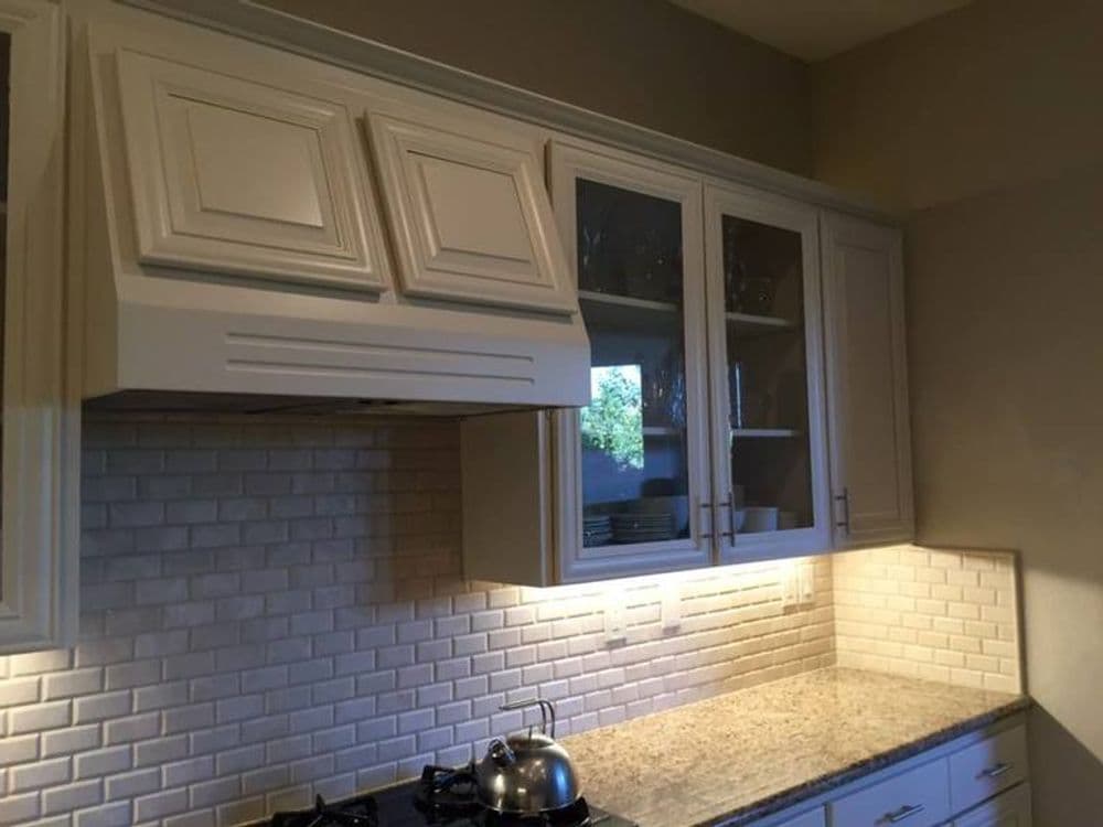Elegant kitchen with white cabinets, granite countertops, and modern backsplash lighting.