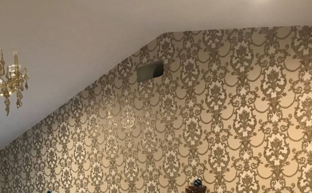 Elegant interior wall with gold damask wallpaper and decorative chandelier.